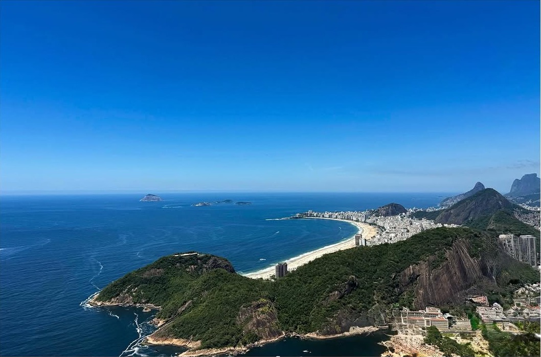 Coastal Views - Aerial photograph of a curved beach and rocky coastline with mountains in the background