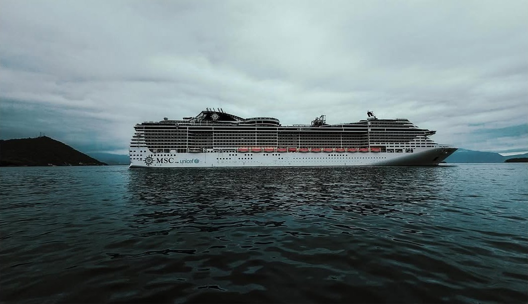 Commercial Spot - MSC cruise ship sailing through calm waters with mountainous coastline under dramatic overcast skies