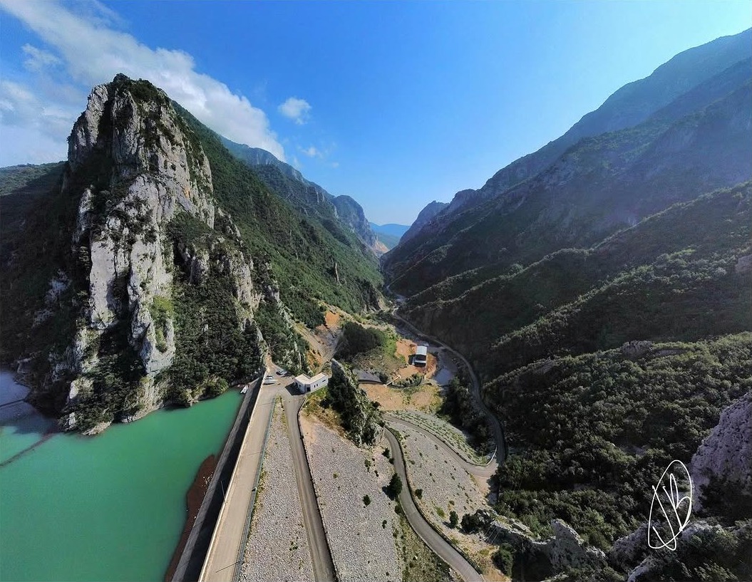 Mountain Expedition - Aerial drone view of a dramatic mountain valley with turquoise reservoir, dam, and winding road through rugged peaks