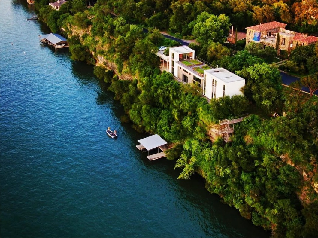 Real Estate Aerial - Aerial drone view of luxury waterfront properties along a lake with modern white architecture, boat docks, and lush green trees
